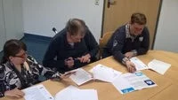 Foto von drei Menschen, die an einem Tisch arbeiten.